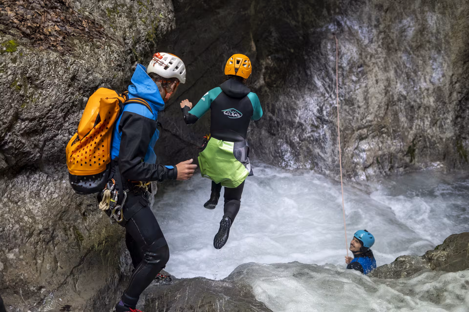 Canyoning guide assists participant jumping into a rushing waterfall pool in Interlaken.