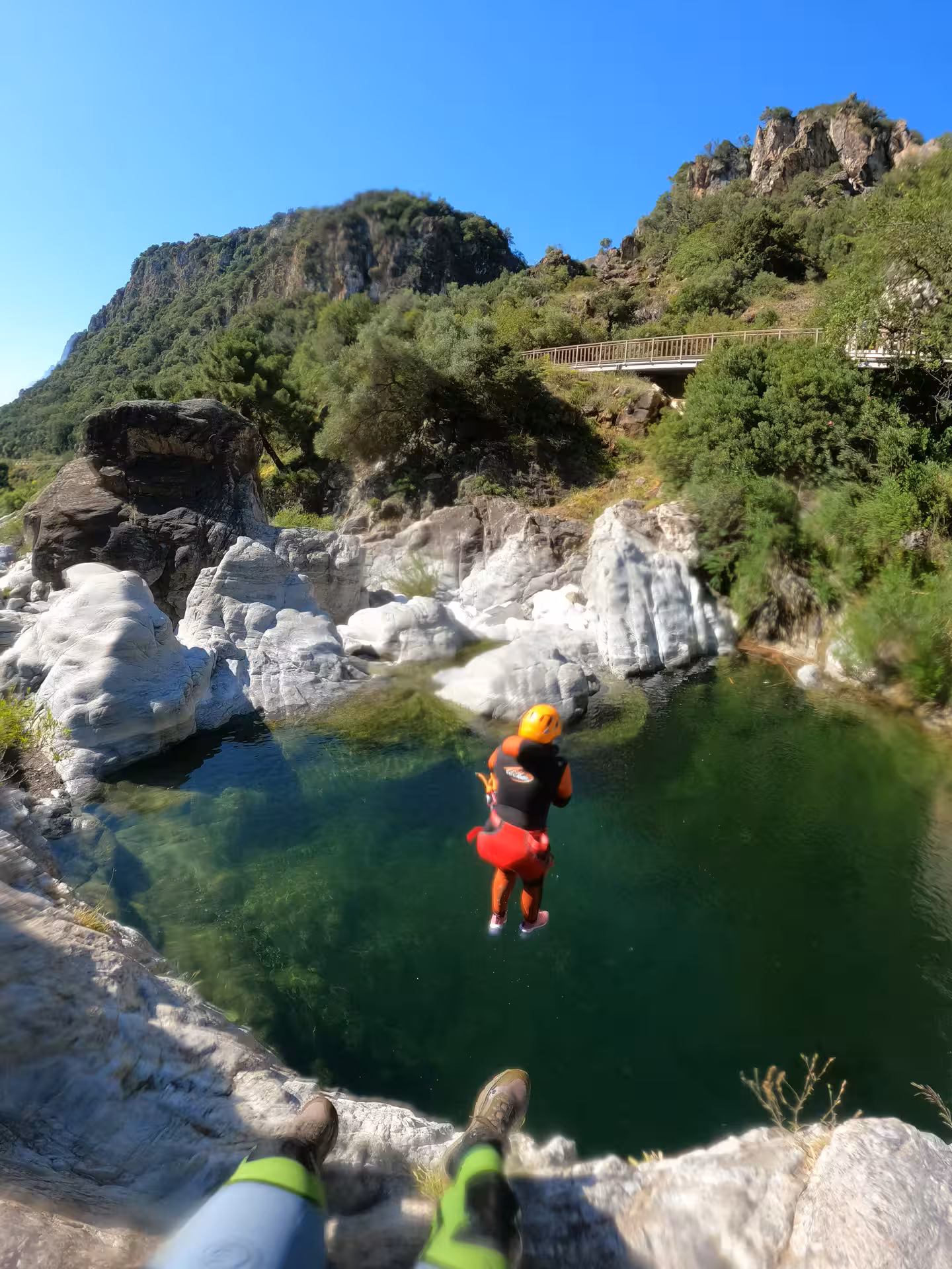 A canyoner in helmet and wetsuit leaps off a rocky cliff into a stunning emerald pool at Guadalmina Canyon on a guided canyoning tour Estepona