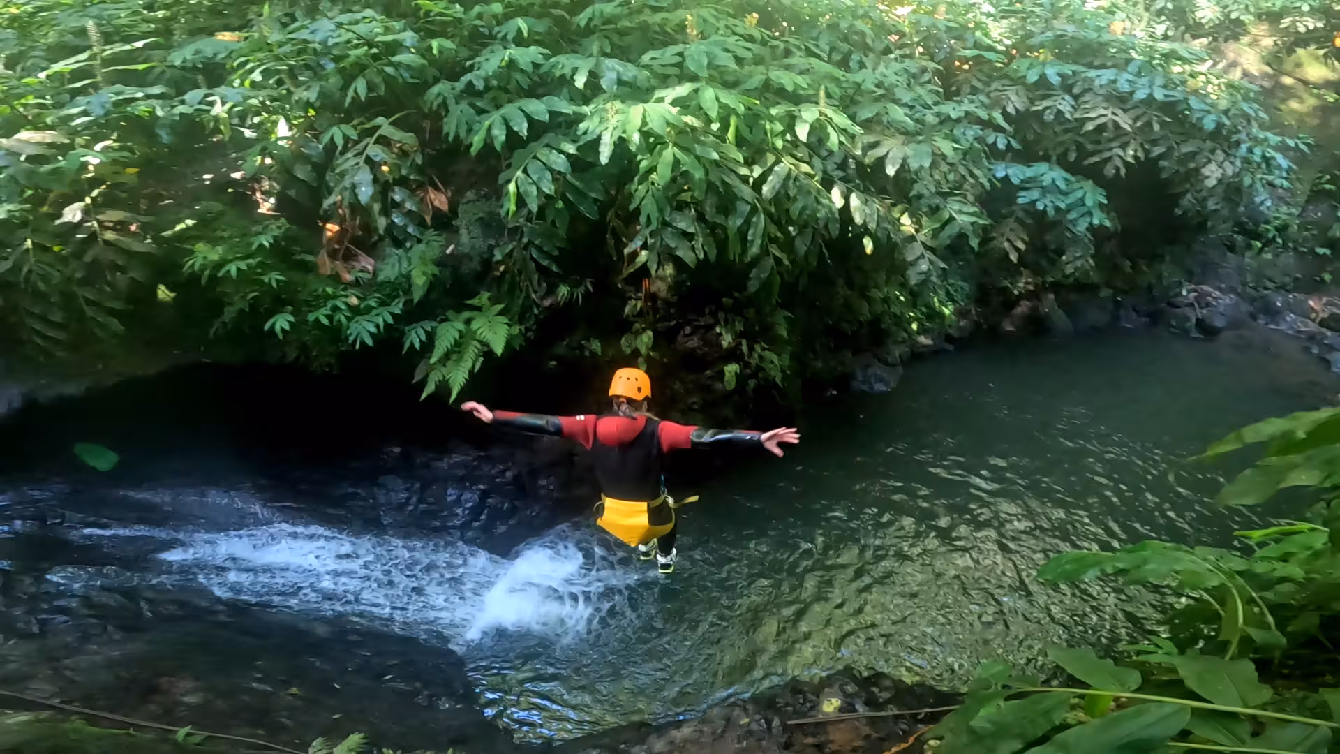 Canyoning jump into a clear jungle pool, helmeted adventurer on guided canyon tour in lush rainforest