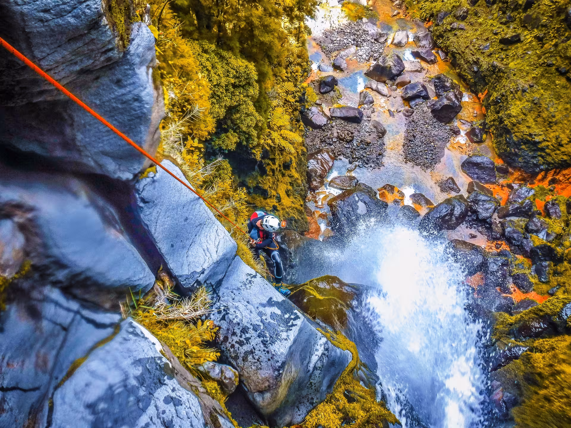 Rappelling down a waterfall on Canyoning Lombadas Praia tour, with rope descent into lush canyon pool