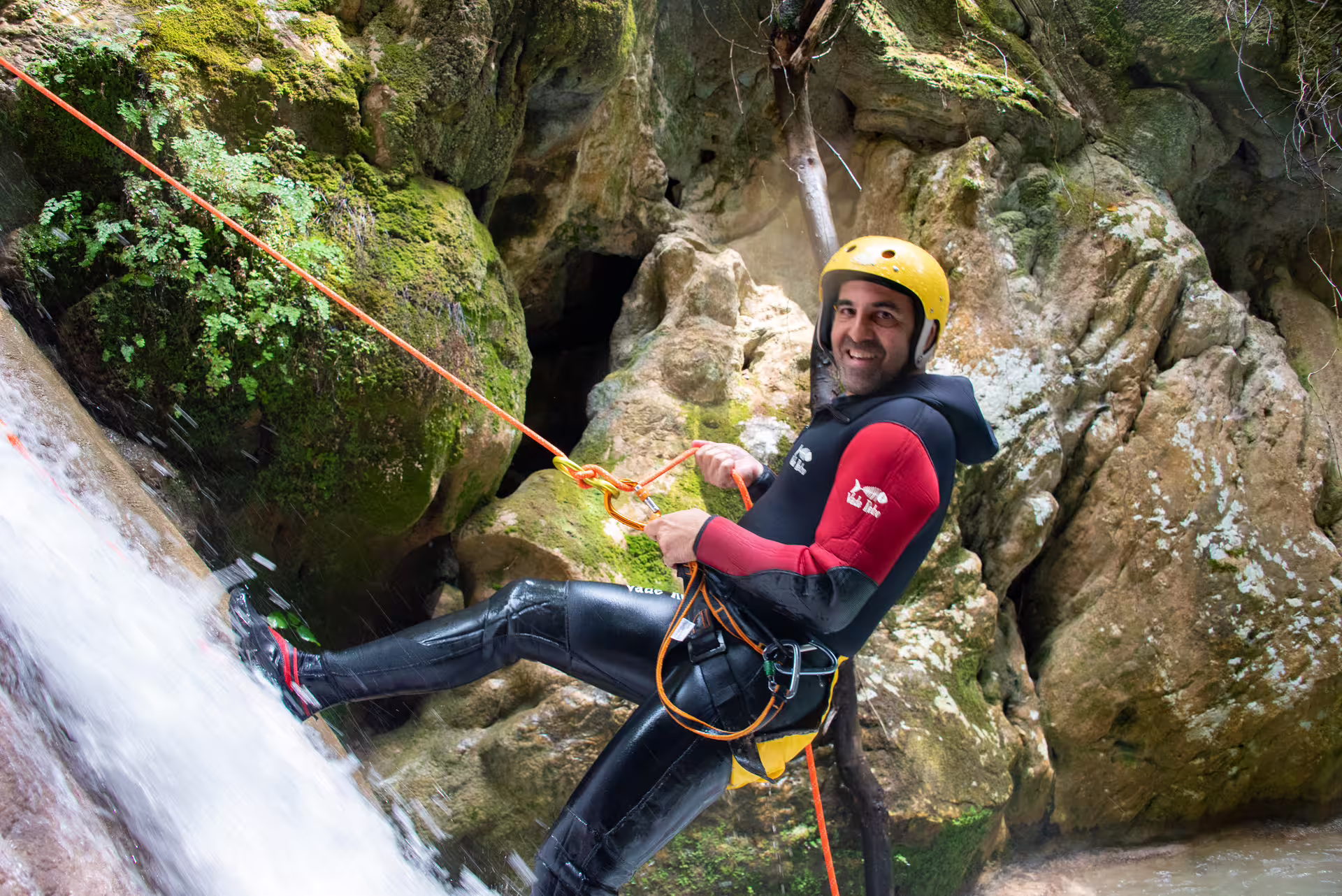 Canyoning guide abseiling beside Neda Waterfalls on rope, wearing helmet and wetsuit in rocky gorge