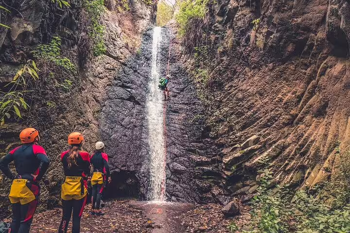 Adventurers canyoning down a waterfall in a lush rainforest, showcasing thrilling outdoor adventure tour in nature.