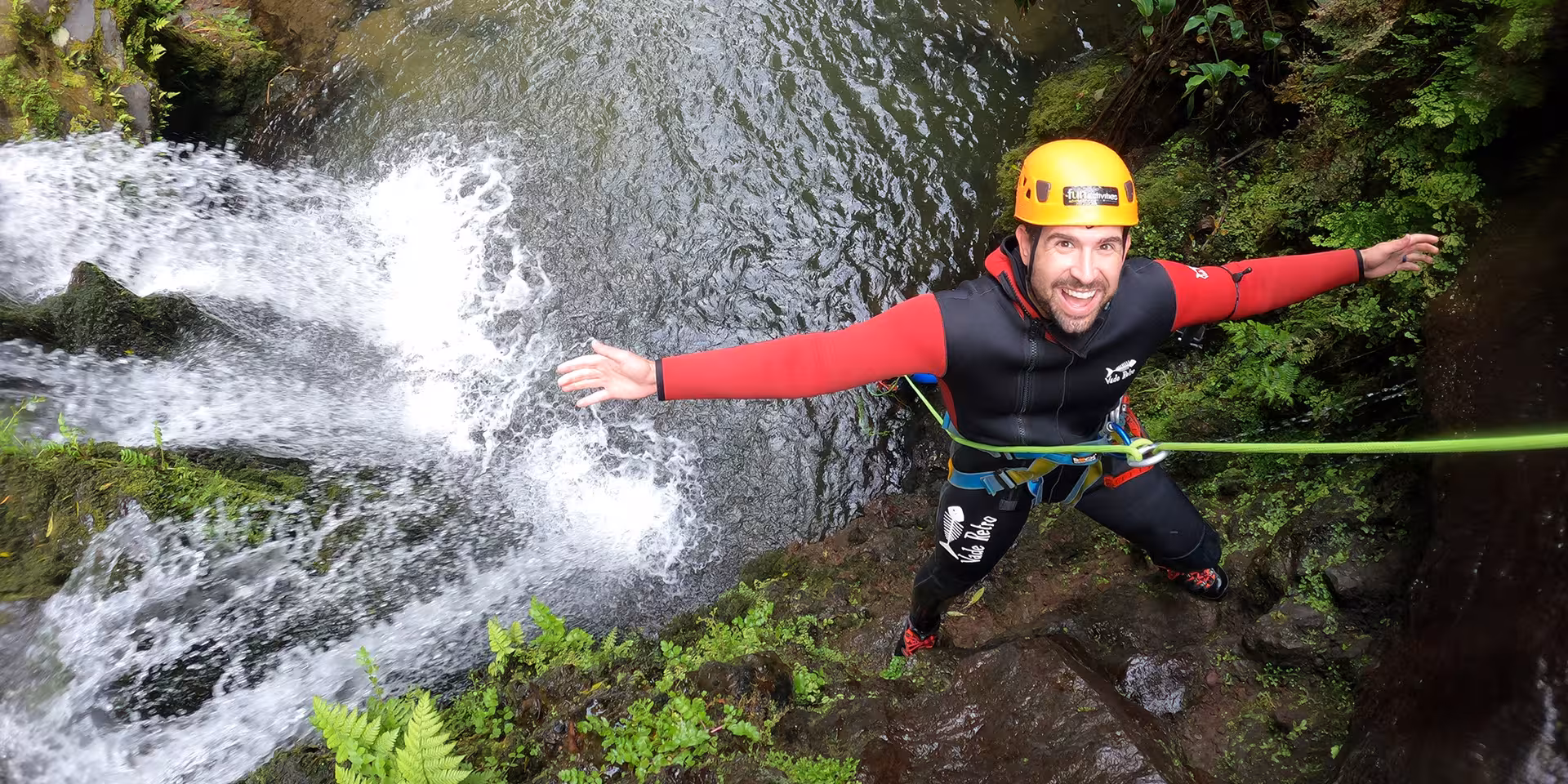 Canyoning rappel beside a waterfall with rope and harness, helmeted climber on guided canyon adventure