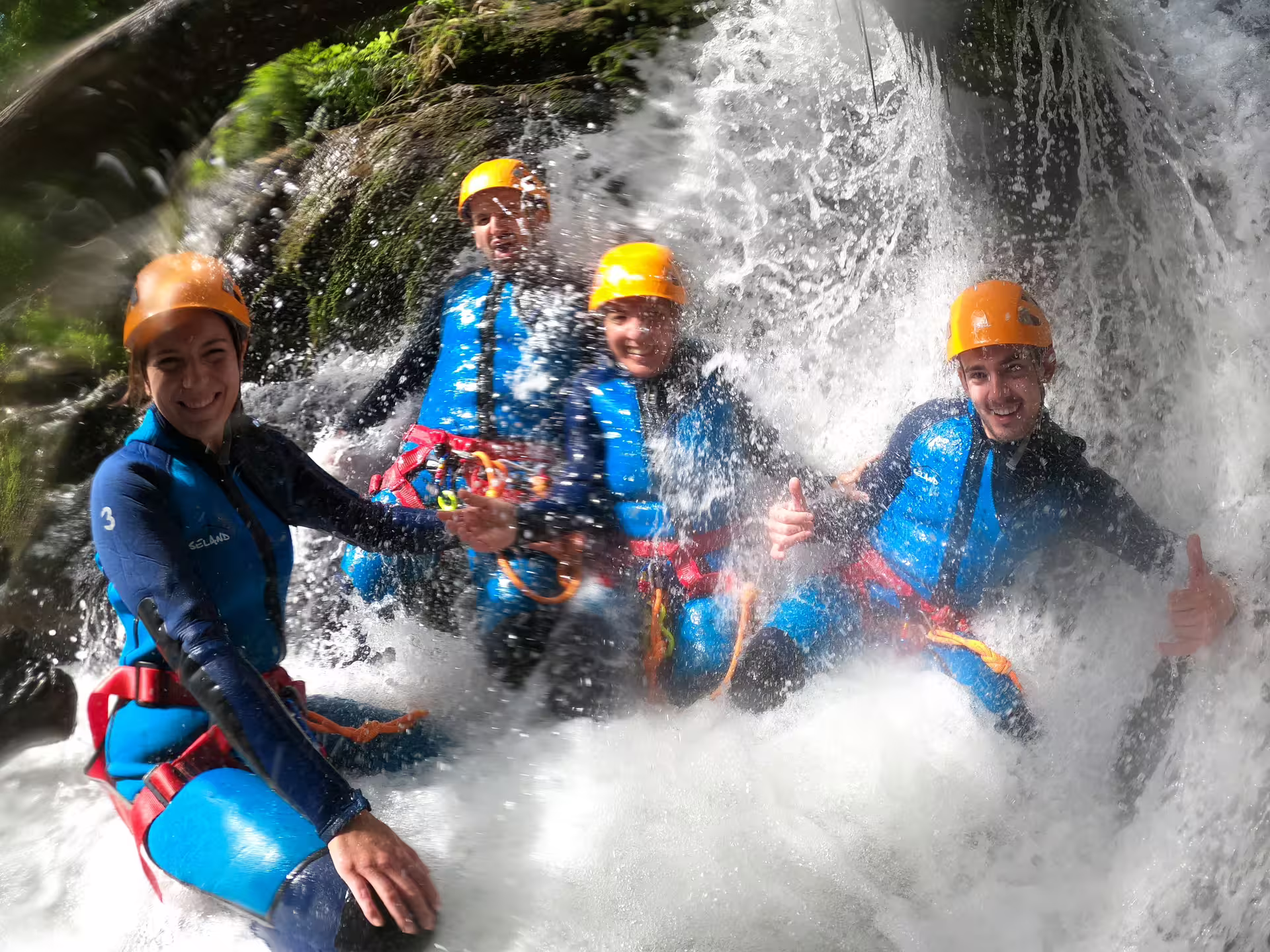 Four smiling canyoners in wetsuits and helmets enjoying a thrilling waterfall splash at Sima del Diablo Ronda guided tour.