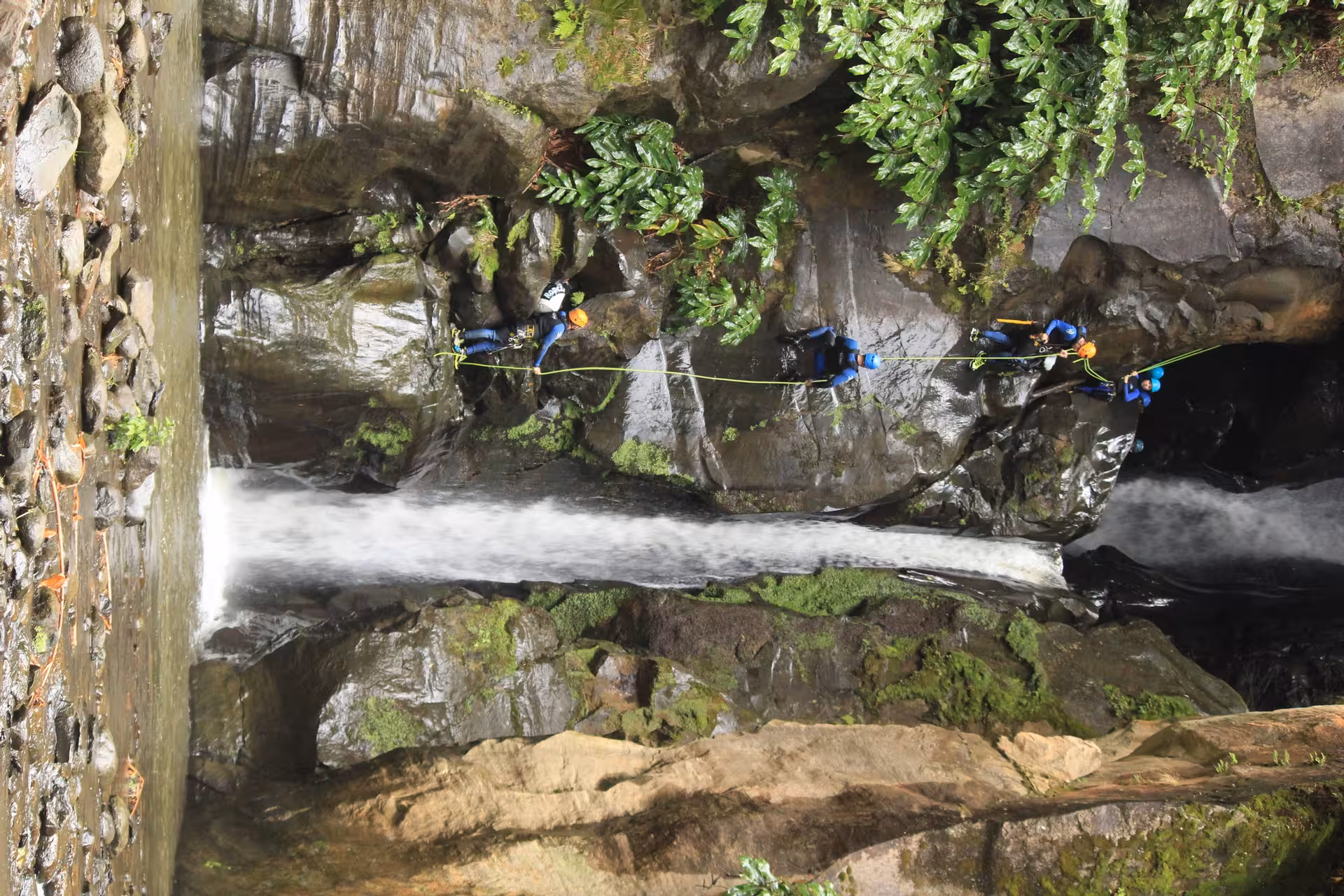 Group canyoning at Salto do Cabrito, Azores, traversing wet canyon walls above waterfall on guided full-day trip