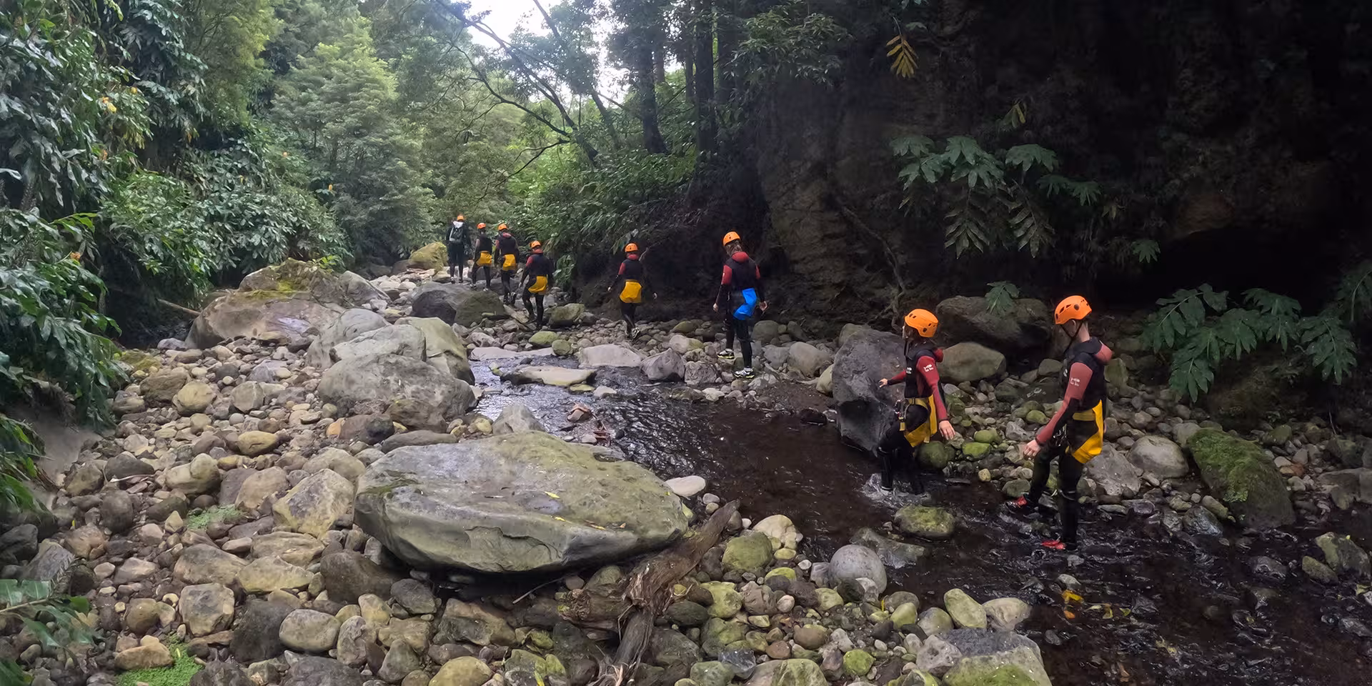 Group canyoning hike through lush Salto do Cabrito canyon riverbed, São Miguel Azores, helmets and wetsuits