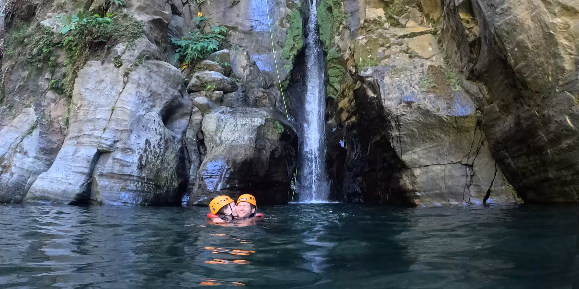 Canyoning at Salto do Cabrito with two helmeted swimmers in a natural pool beneath the waterfall
