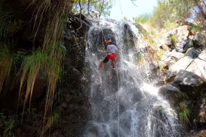 Adventurer canyoning down a scenic waterfall in Sierra Bermeja, Estepona, surrounded by lush greenery and rugged rocks.