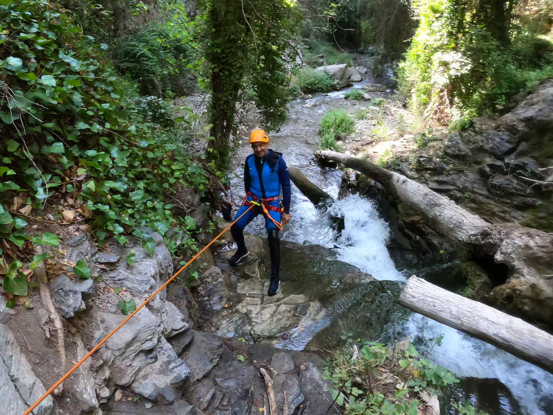 A harnessed canyoning adventurer navigating rocky canyon terrain with a rope beside a rushing stream at Sima del Diablo Ronda.