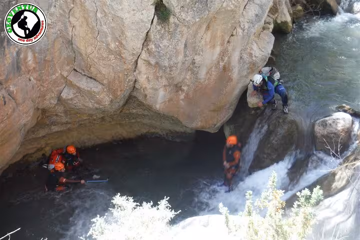 Canyoning Teruel group abseiling into a narrow gorge pool under a rock overhang with rushing water