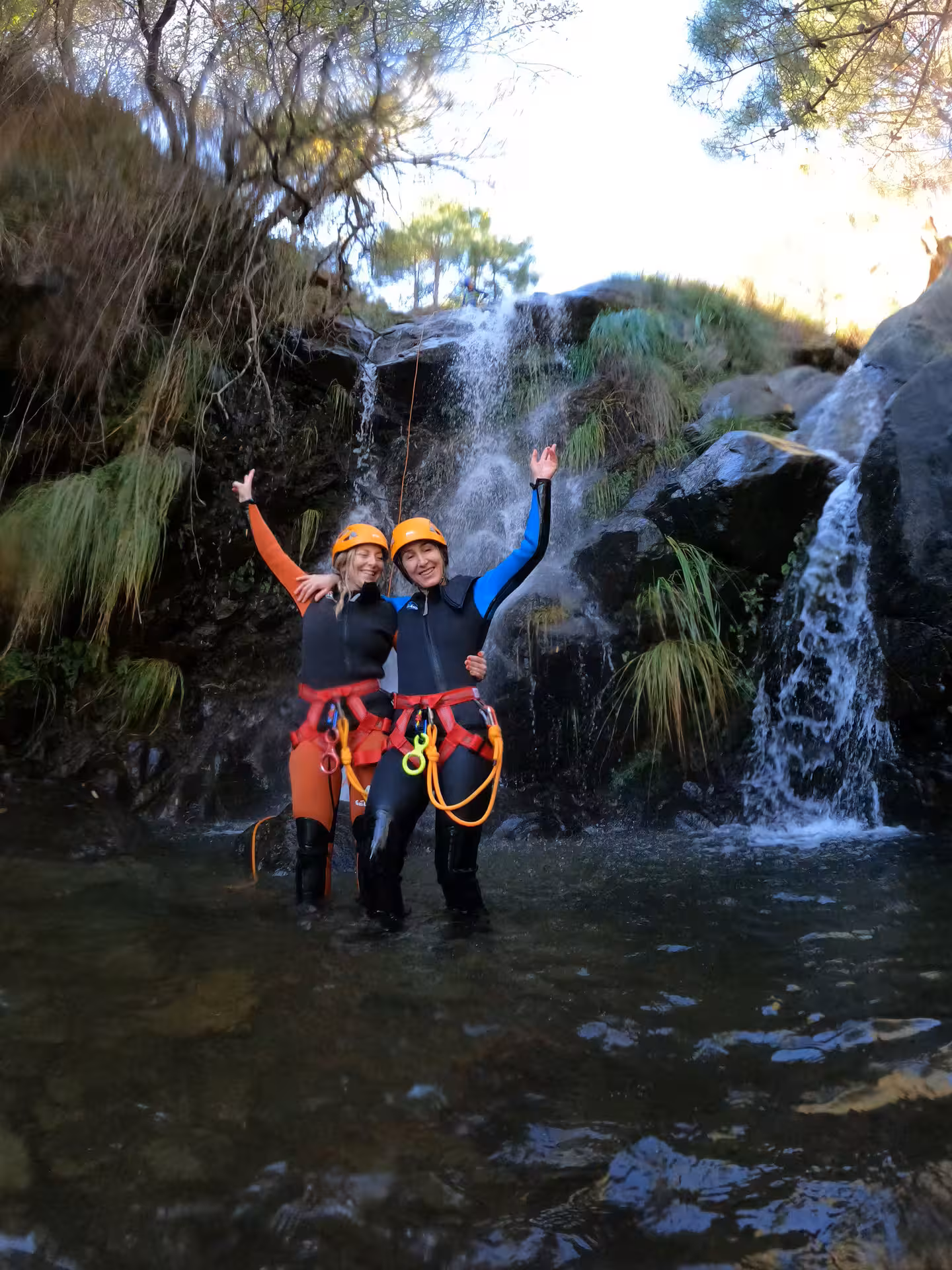 Two happy canyoning participants in wetsuits and helmets celebrate near a waterfall in Sierra Bermeja Estepona Spain.