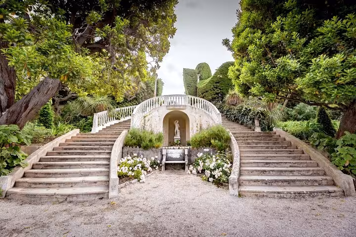 Elegant double staircase with white balustrade and statue niche surrounded by lush gardens in Cap Ferrat