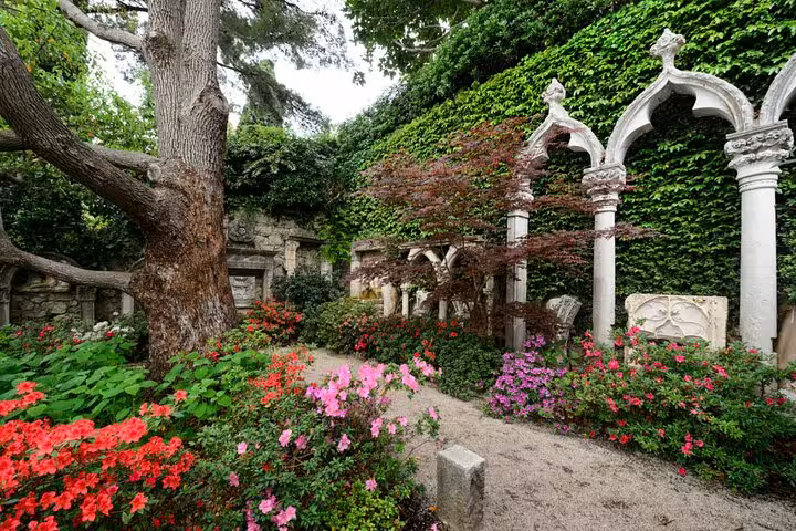Ornate white stone arches covered in ivy with colorful azalea gardens at Villa Kerylos, Cap Ferrat