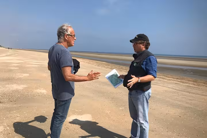 Two men discussing a map on a sandy beach near Cap Frehel, Brittany, France
