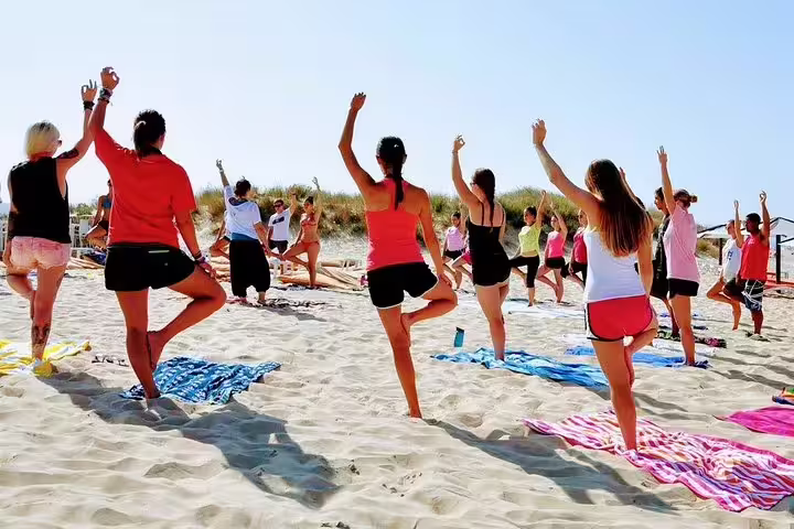 Participants enjoying a beach yoga session under clear skies at Caparica, highlighting surf and wellness retreats in Portugal.