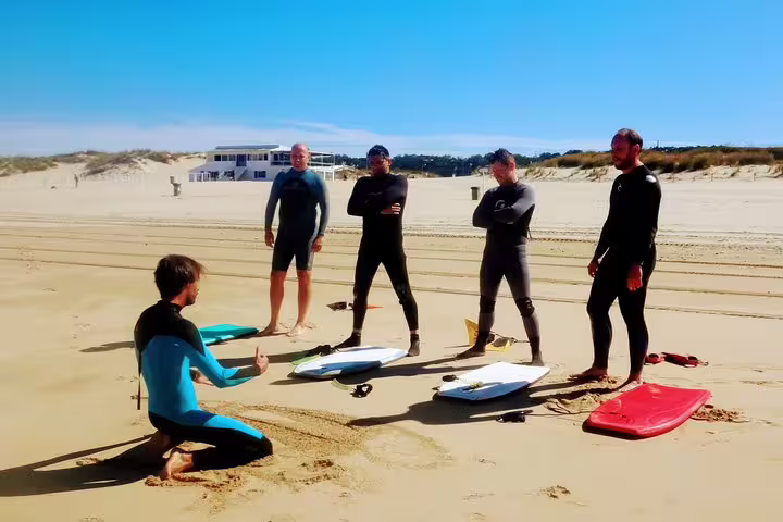 Group of bodyboarders in wetsuits receiving instruction on Caparica Beach, perfect for adventure and water sports enthusiasts.