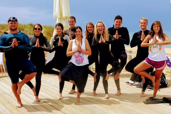 Group enjoying yoga on a sunny Caparica beach, dressed in wetsuits, combining surf and wellness for a rejuvenating experience.