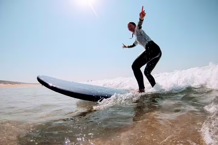 Person surfing a wave on a sunny day at Caparica, Portugal, enjoying an exciting surf and yoga retreat experience.