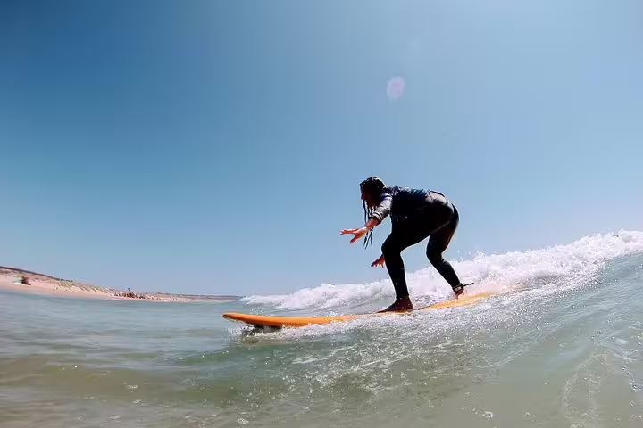 Person surfing a wave on a sunny day at Caparica beach, ideal for surf and yoga enthusiasts seeking adventure and relaxation.
