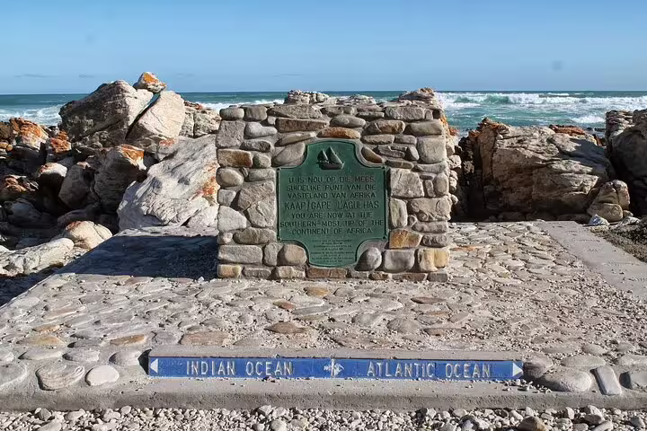 Stone monument marking the meeting point of the Indian and Atlantic Oceans at Cape Agulhas with rocky coast.