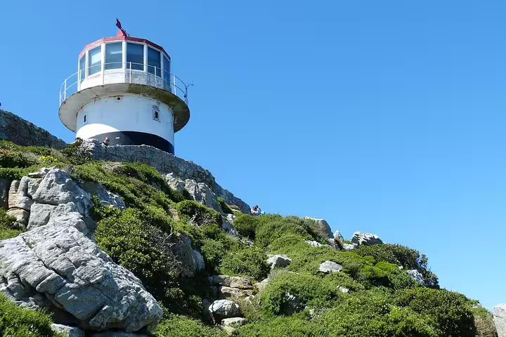 Iconic lighthouse atop rocky cliffs under a clear blue sky at Cape of Good Hope, ideal for scenic tours from Cape Town.