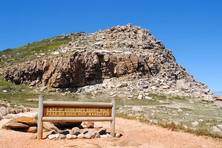 The Cape of Good Hope Scenic Walk sign against a rocky hillside under a clear blue sky in Cape Town, South Africa.