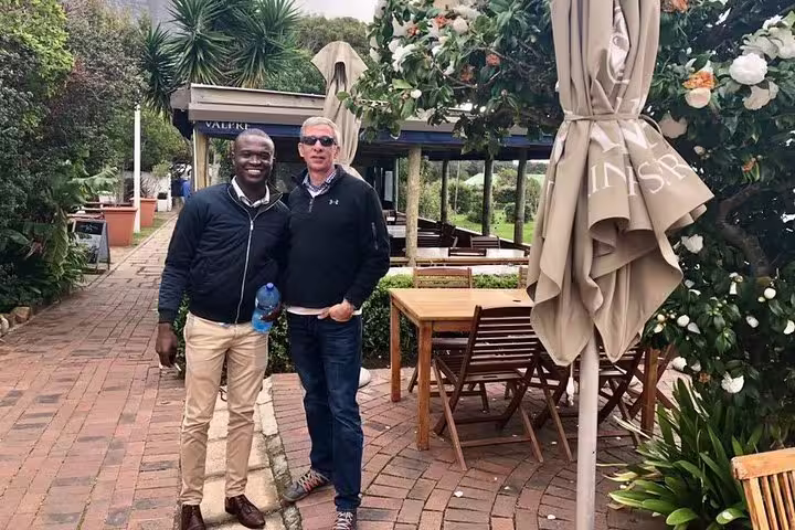 Two smiling men posing on a scenic outdoor patio at a cafe stop during Cape of Good Hope tour from Cape Town.