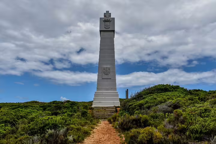 Scenic view of the Cape of Good Hope monument surrounded by lush greenery and a cloudy sky backdrop.