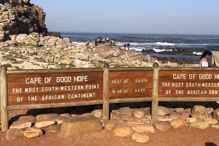 Scenic view of Cape of Good Hope with iconic sign, rocky coastline, and tourists enjoying the vibrant South African landscape.