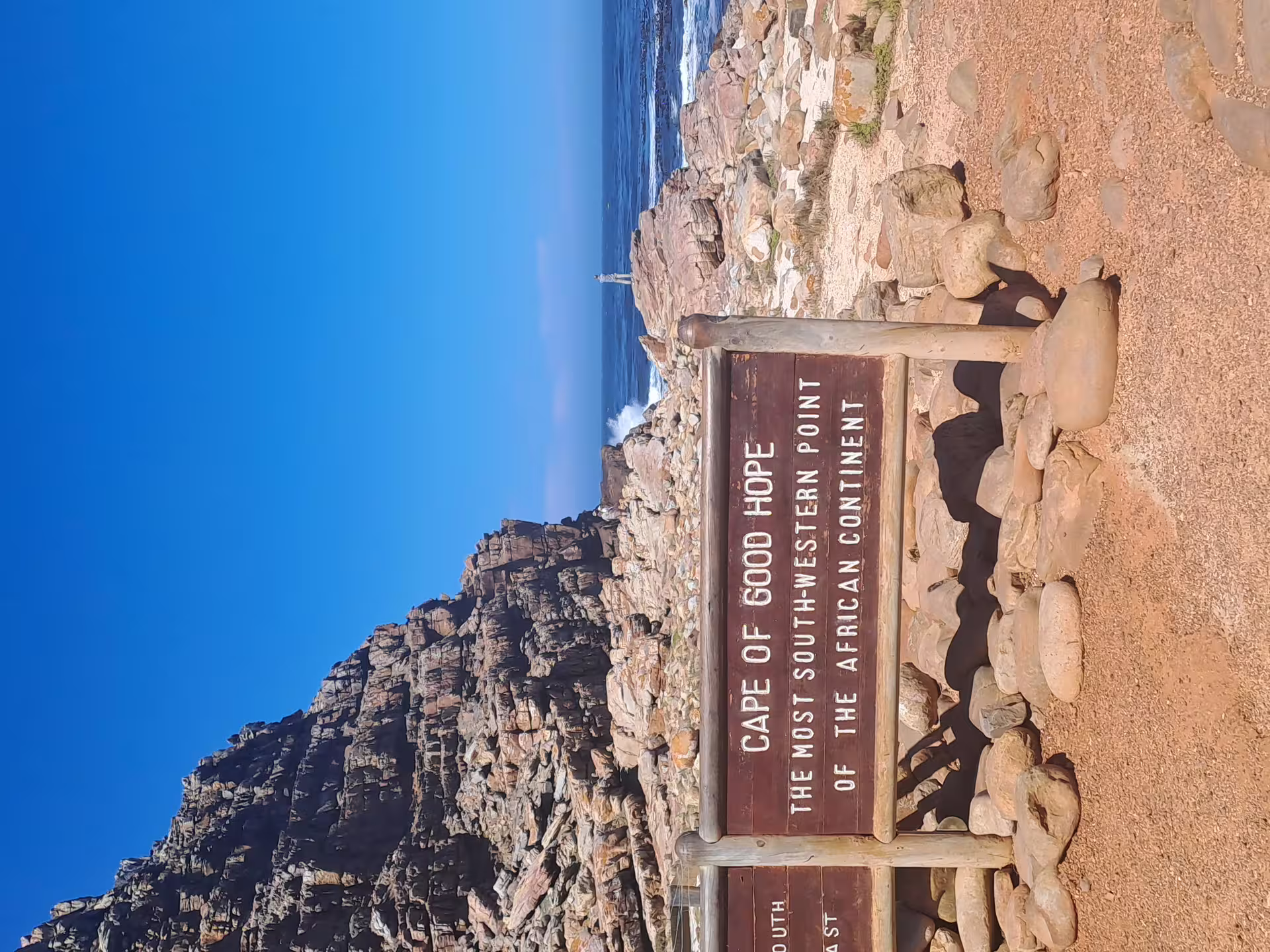 Sign at Cape of Good Hope marking the southwestern point of Africa, with rocky cliffs and ocean backdrop.
