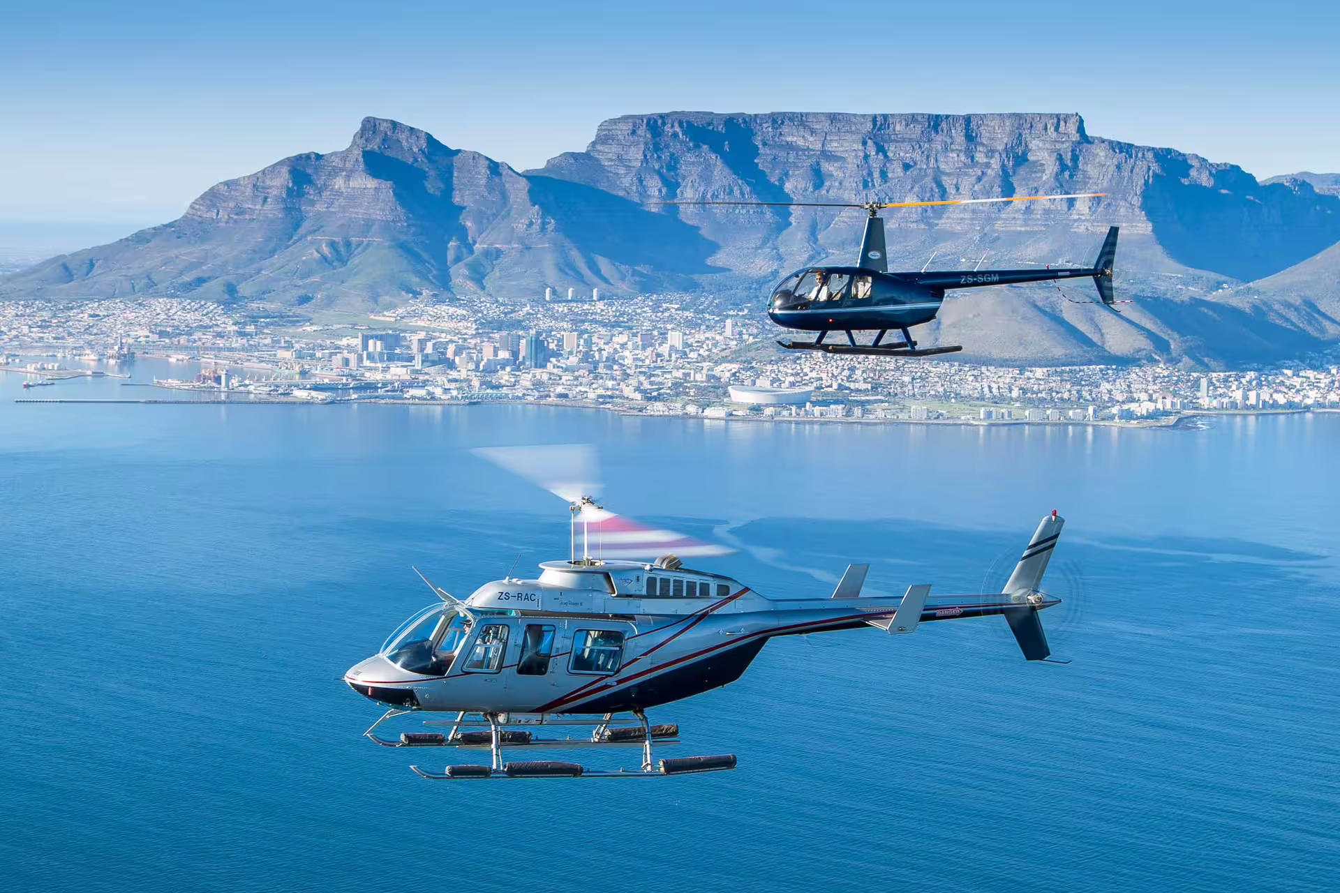 Helicopters flying over Cape Town's coastline with Table Mountain in background, highlighting the Cape Point Tour adventure.