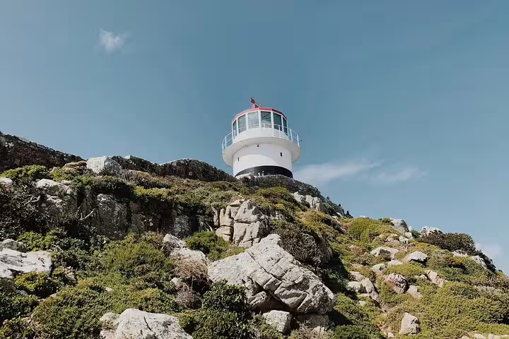 Scenic view of Cape Point Lighthouse atop rocky cliffs under a clear blue sky on the Cape Peninsula Tour.