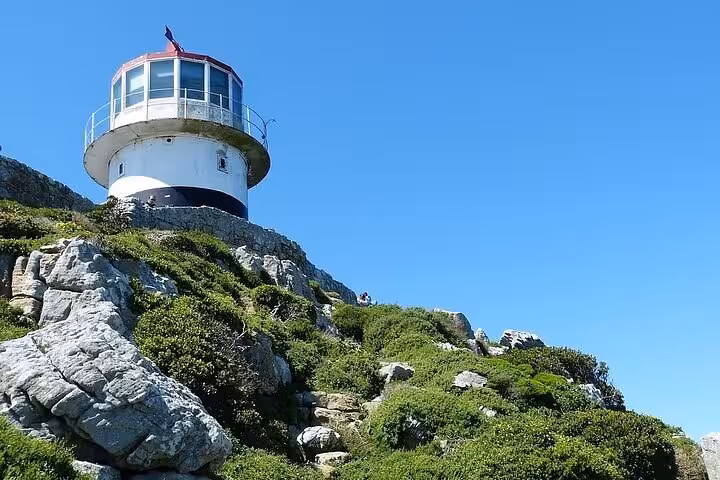 Scenic view of a lighthouse perched on rocky cliffs at Cape Point under clear blue skies.