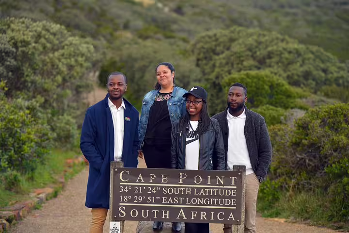 Group of tourists posing at Cape Point sign, South Africa, surrounded by lush greenery on a private day tour.