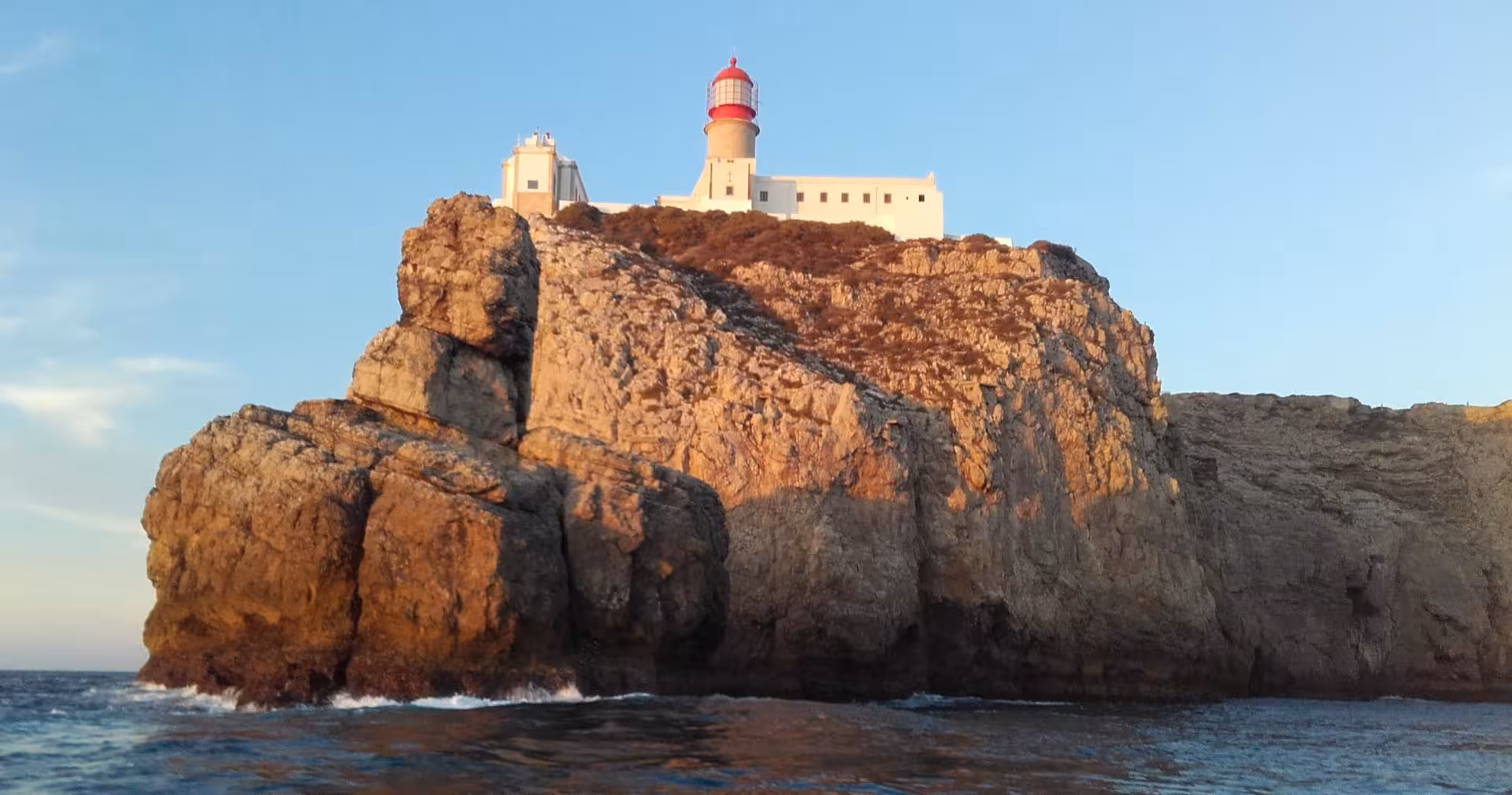 Stunning view of Cape St. Vincent lighthouse perched on rugged cliffs, basking in golden hour light over the Atlantic Ocean.