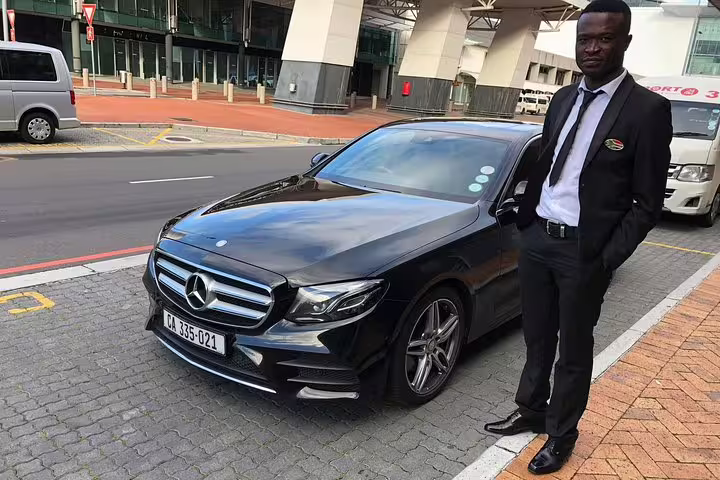 Professional driver standing beside a luxury black Mercedes-Benz for Cape Town airport transfer service.