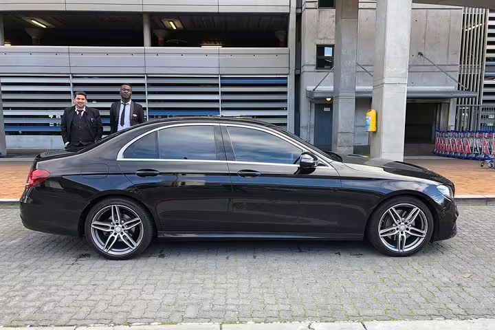 Side view of a sleek black Mercedes-Benz with two drivers ready for Cape Town airport transfer.