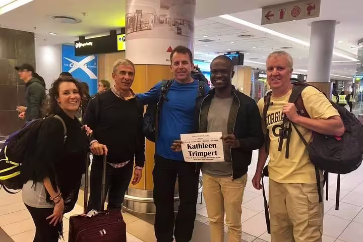 Friendly airport transfer staff greeting travelers with a welcome sign at Cape Town International Airport.
