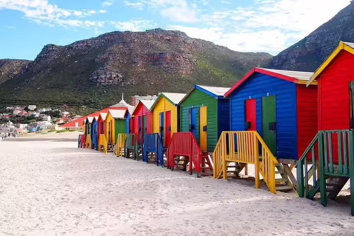 Colorful beach huts lined up along the sandy shore with mountains in the background in Cape Town.