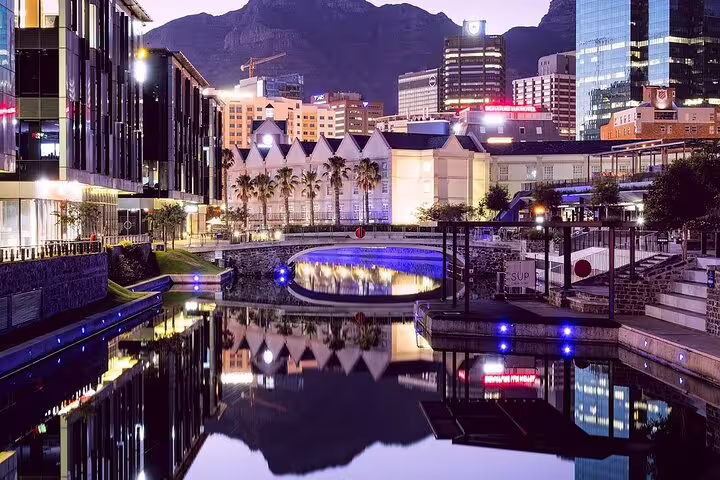 Twilight view of Cape Town's vibrant waterfront district reflecting on calm waters with Table Mountain backdrop.