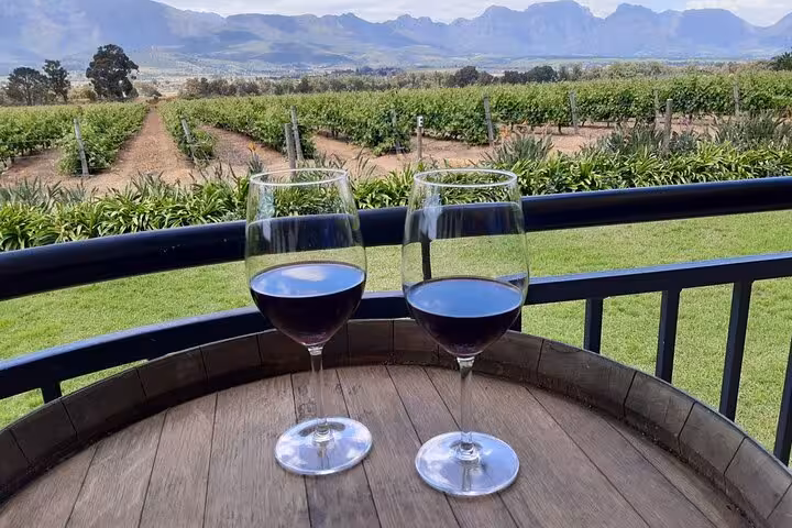 Two glasses of red wine on a barrel with a stunning view of lush vineyards and mountains near Cape Town.