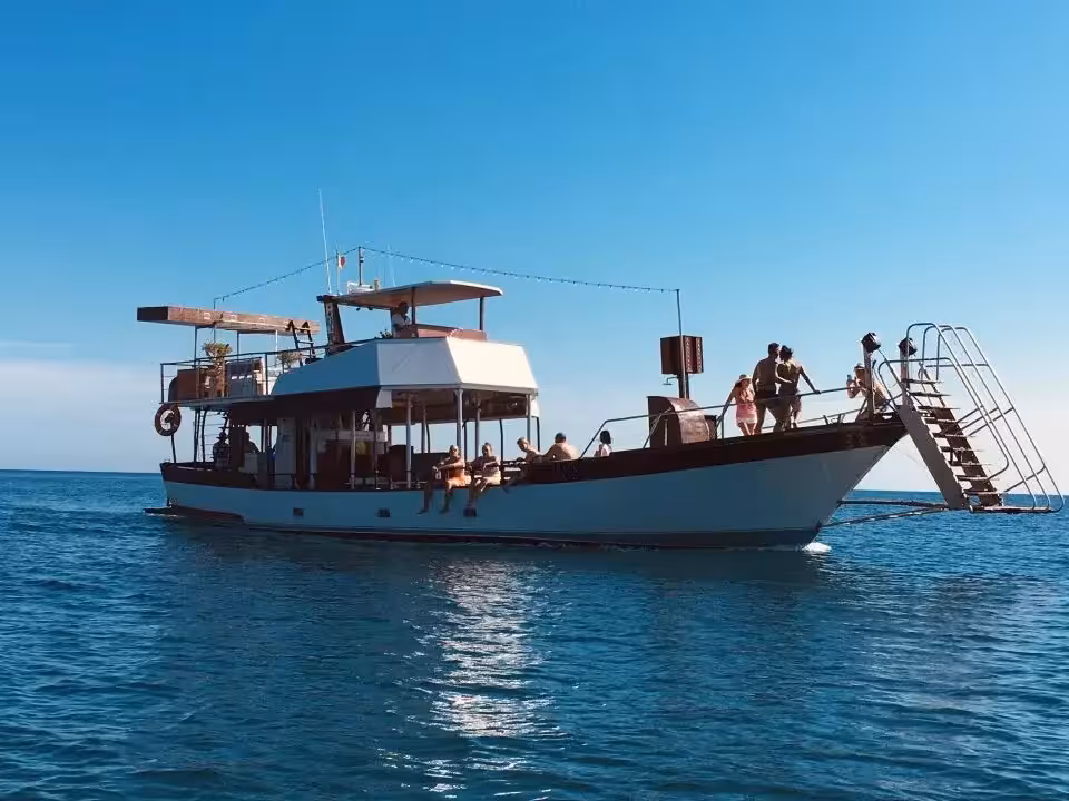 Tourists enjoy a sunny day on a boat tour in Capo Rizzuto marine protected area, with clear blue waters and sky.