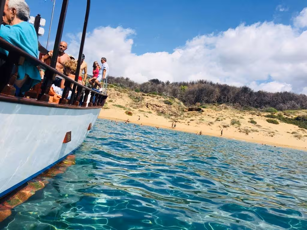 Tourists enjoy a scenic boat tour near golden sands at Capo Rizzuto marine protected area under clear blue skies.