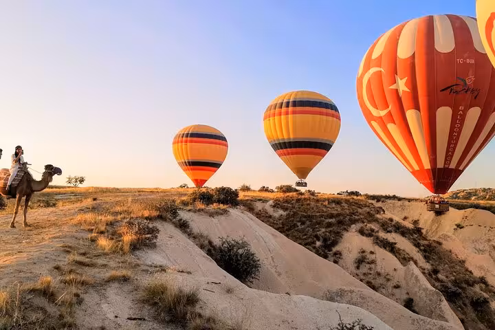 Cappadocia camel ride tour at sunrise with hot air balloons floating above the fairy chimneys in Göreme