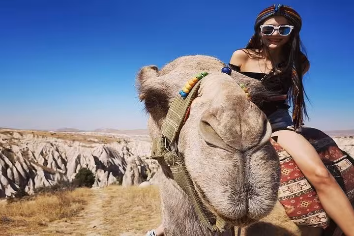 Traveler on Cappadocia camel ride tour with close-up camel, overlooking fairy chimney valleys under blue sky