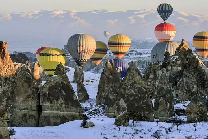 Colorful hot air balloons soar over snowy Cappadocia landscapes, offering a magical winter adventure in Turkey.