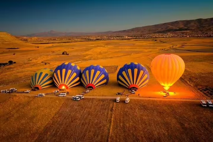 Vibrant hot air balloons prepare for takeoff at sunrise in Cappadocia's stunning landscape, ready for a champagne flight.