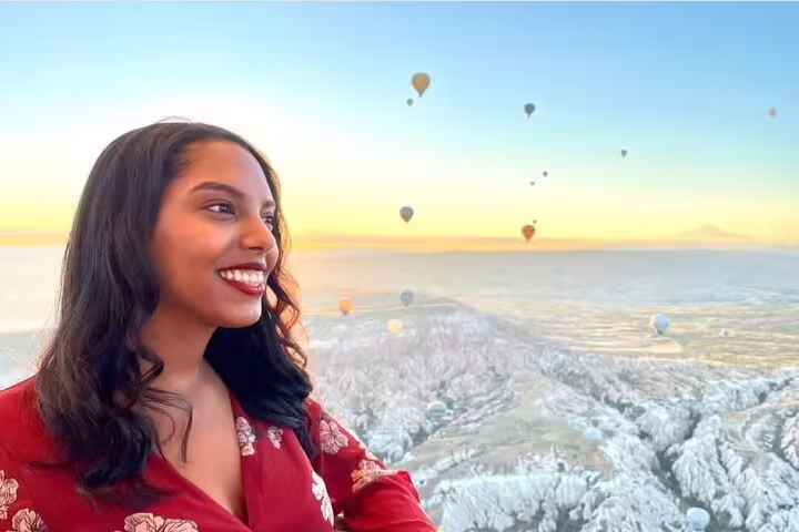 A woman gazes at Cappadocia's scenic landscape, with hot air balloons dotting the sunrise sky, creating a magical view.