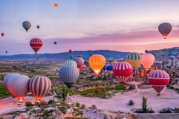 Vibrant hot air balloons soar over Cappadocia's surreal landscape at sunrise, offering a magical champagne experience.