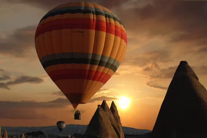 A hot air balloon drifts over Cappadocia's mystical landscape at sunset, highlighting the region's stunning natural beauty.